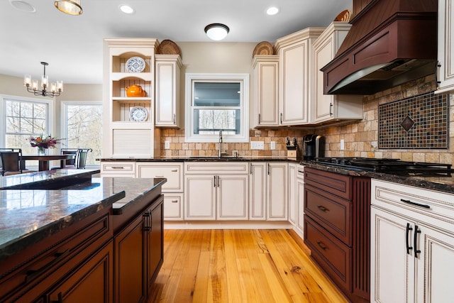 kitchen featuring custom exhaust hood, an inviting chandelier, open shelves, backsplash, and a sink