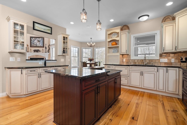 kitchen featuring a chandelier, tasteful backsplash, glass insert cabinets, and a sink