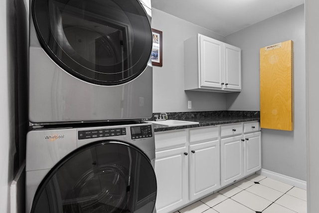 laundry room with stacked washer and dryer, light tile patterned floors, a sink, baseboards, and cabinet space