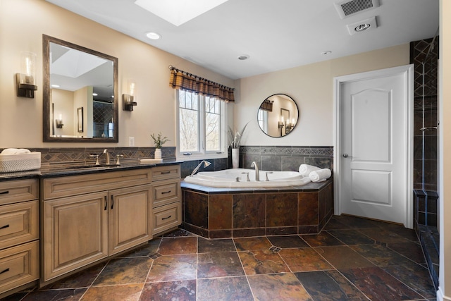 full bathroom with a skylight, a bath, vanity, stone tile floors, and visible vents