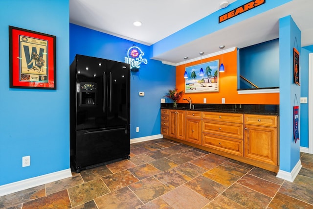 kitchen featuring a sink, brown cabinets, black fridge with ice dispenser, stone tile floors, and baseboards