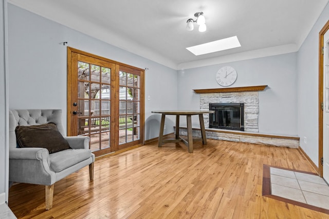 living area featuring a skylight, a stone fireplace, baseboards, and light wood finished floors