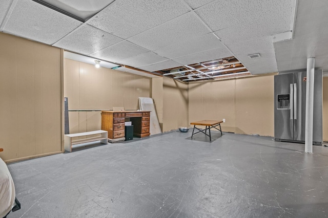 basement featuring visible vents, a paneled ceiling, and stainless steel fridge with ice dispenser