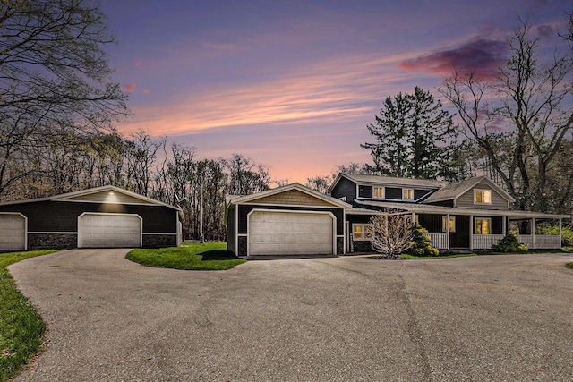 view of front of property with covered porch, a detached garage, aphalt driveway, and stone siding