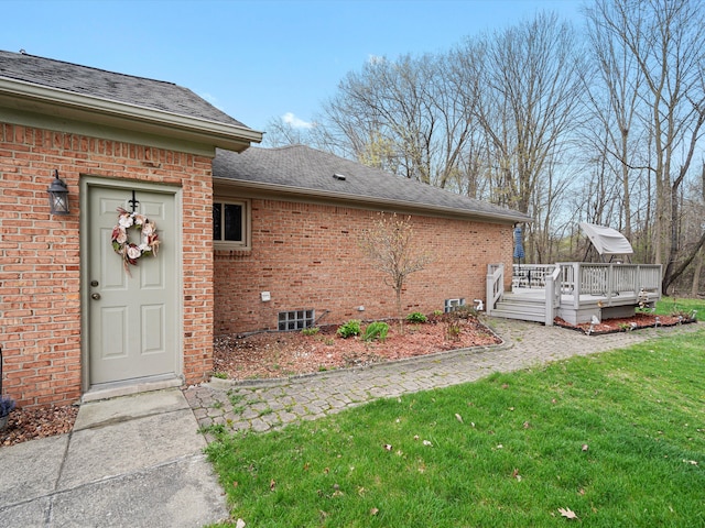exterior space featuring a yard, a deck, brick siding, and roof with shingles