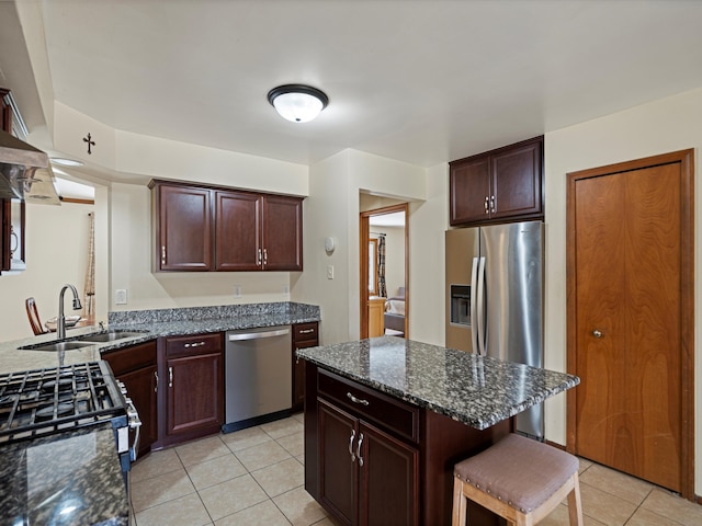 kitchen featuring light tile patterned flooring, a breakfast bar, dark stone counters, a sink, and stainless steel appliances