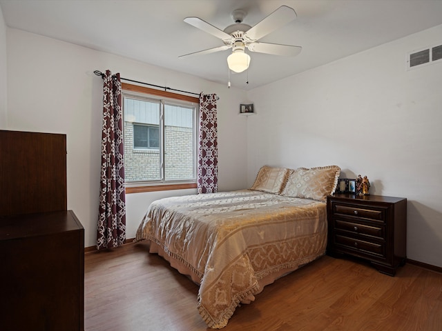 bedroom featuring a ceiling fan, baseboards, visible vents, and wood finished floors