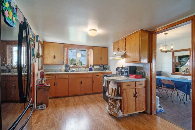 kitchen featuring black appliances, light countertops, under cabinet range hood, and light wood-style floors