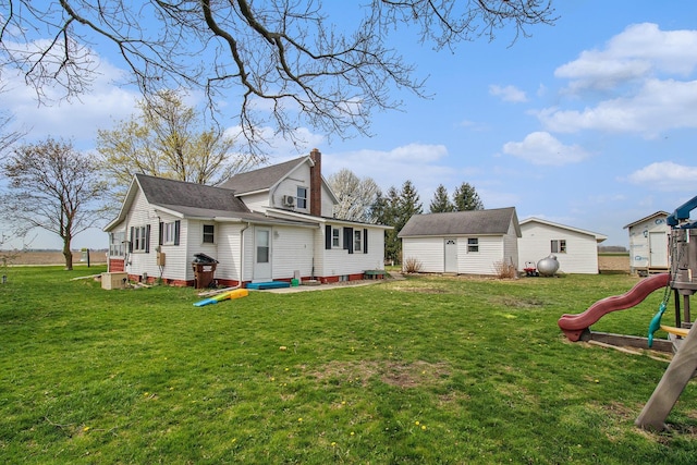 back of house with a lawn, an outdoor structure, a chimney, and a playground