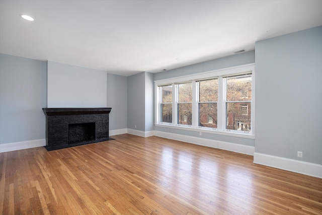 unfurnished living room with recessed lighting, baseboards, a fireplace with flush hearth, and light wood finished floors