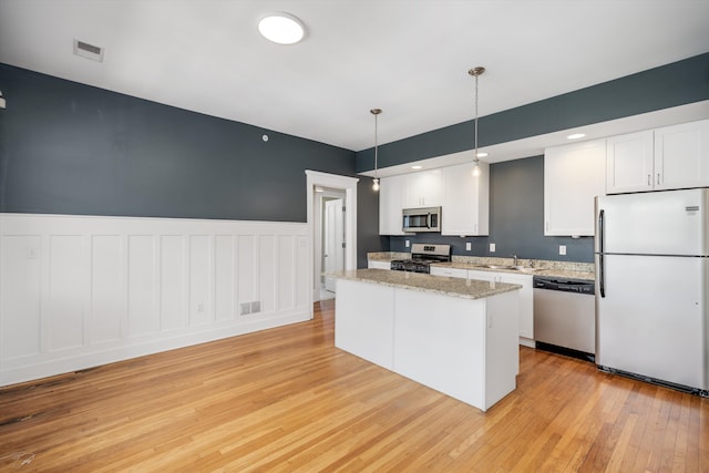 kitchen featuring white cabinets, appliances with stainless steel finishes, wainscoting, light wood finished floors, and a kitchen island