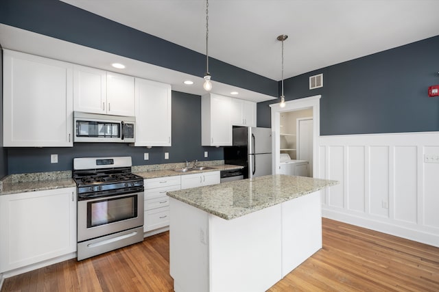 kitchen featuring visible vents, appliances with stainless steel finishes, light wood-type flooring, a sink, and washer / dryer