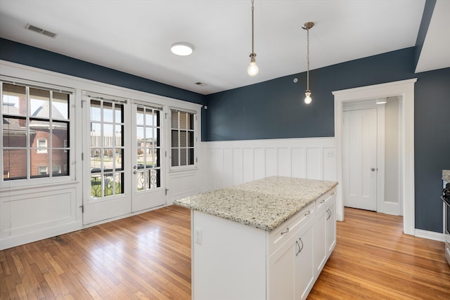 kitchen with visible vents, light wood-style floors, plenty of natural light, and a wainscoted wall