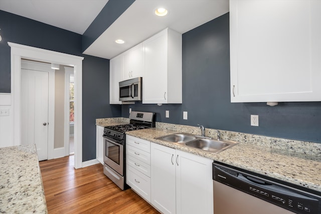 kitchen with appliances with stainless steel finishes, light wood-type flooring, a sink, recessed lighting, and white cabinetry