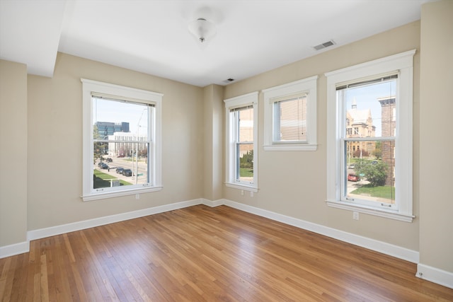 empty room with light wood-style floors, baseboards, a wealth of natural light, and visible vents