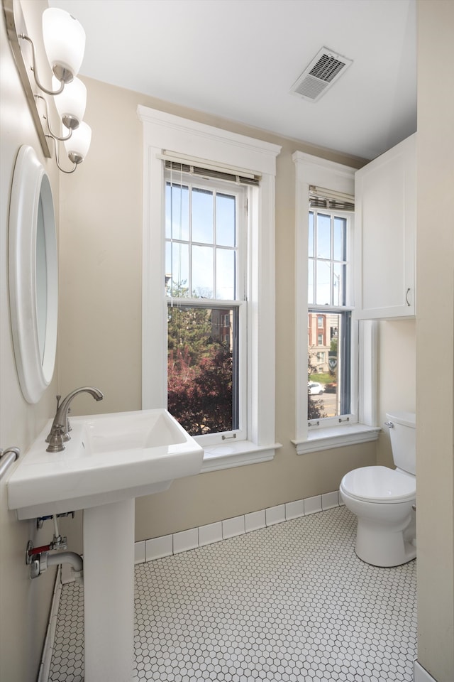 half bath with visible vents, a sink, tile patterned flooring, and toilet