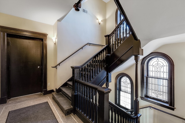 stairway featuring visible vents, baseboards, and a towering ceiling