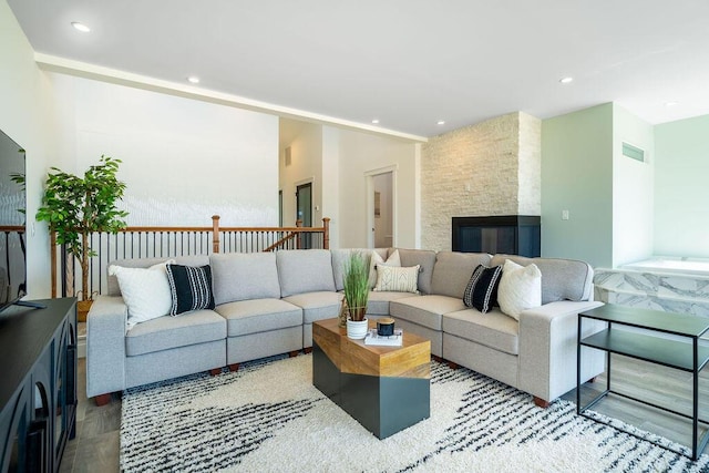 living room featuring recessed lighting, a stone fireplace, and wood finished floors