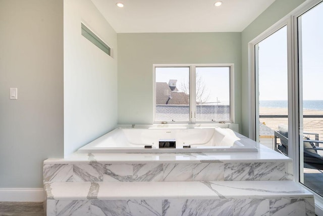 bathroom featuring recessed lighting, a water view, a bath, and a healthy amount of sunlight