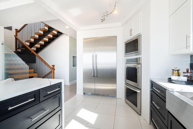 kitchen featuring dark cabinets, built in appliances, light tile patterned floors, and white cabinetry