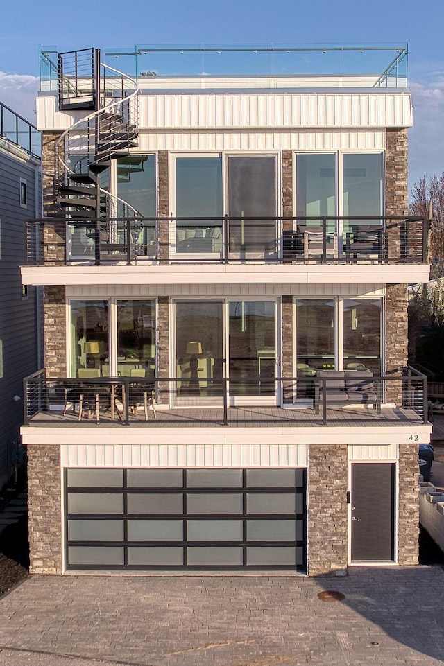 contemporary house with stone siding, an attached garage, decorative driveway, and a balcony