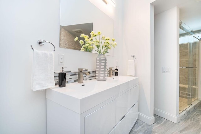 full bathroom with a sink, double vanity, baseboards, backsplash, and a stall shower