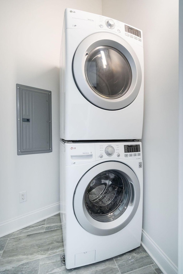 washroom featuring stacked washing maching and dryer, baseboards, electric panel, and laundry area