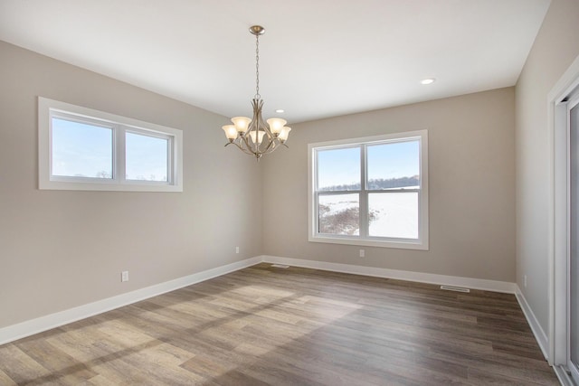 empty room featuring baseboards, recessed lighting, wood finished floors, and a notable chandelier