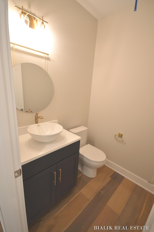 half bath featuring toilet, vanity, wood finished floors, and baseboards