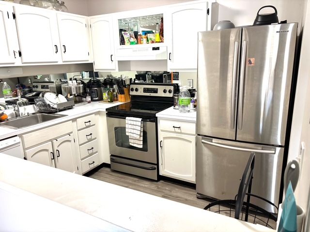 kitchen featuring wood finished floors, stainless steel appliances, under cabinet range hood, light countertops, and a sink