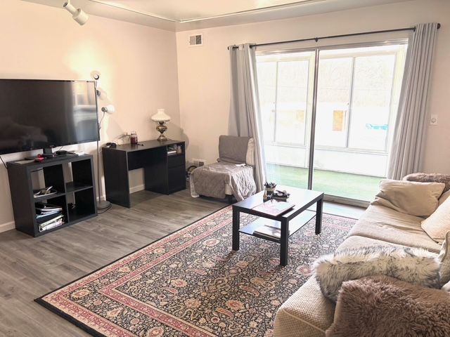 living room with baseboards, visible vents, and wood finished floors
