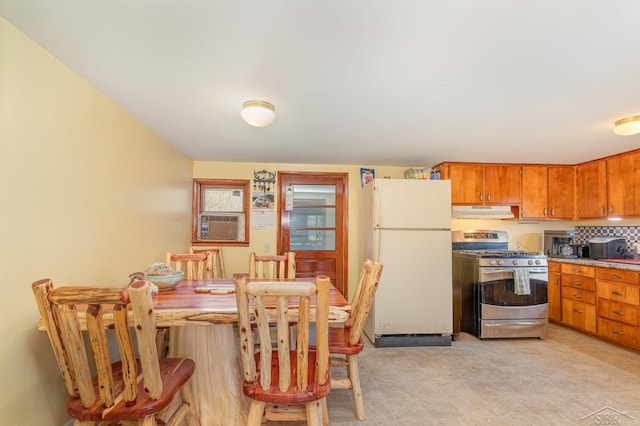 kitchen with brown cabinets, gas range, freestanding refrigerator, under cabinet range hood, and cooling unit