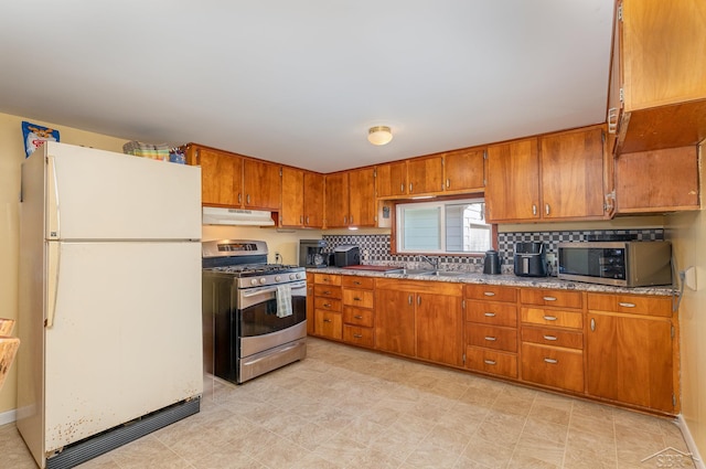 kitchen with decorative backsplash, brown cabinetry, stainless steel appliances, under cabinet range hood, and a sink