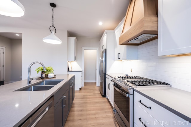 kitchen with a sink, stainless steel appliances, custom range hood, white cabinetry, and pendant lighting