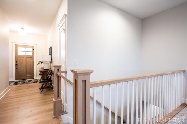 hall featuring light wood finished floors, an upstairs landing, and baseboards