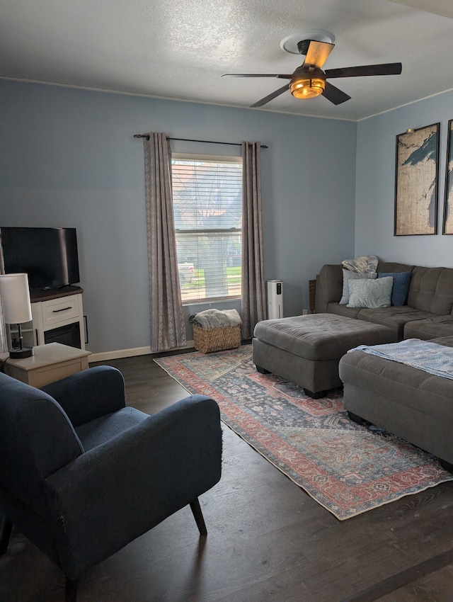 living room with a textured ceiling, ceiling fan, wood finished floors, and baseboards