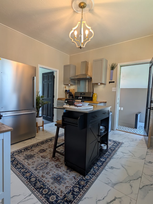 kitchen featuring wall chimney range hood, freestanding refrigerator, an inviting chandelier, marble finish floor, and hanging light fixtures