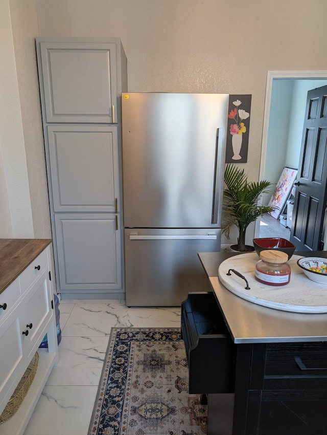 kitchen with butcher block counters, marble finish floor, white cabinets, and freestanding refrigerator