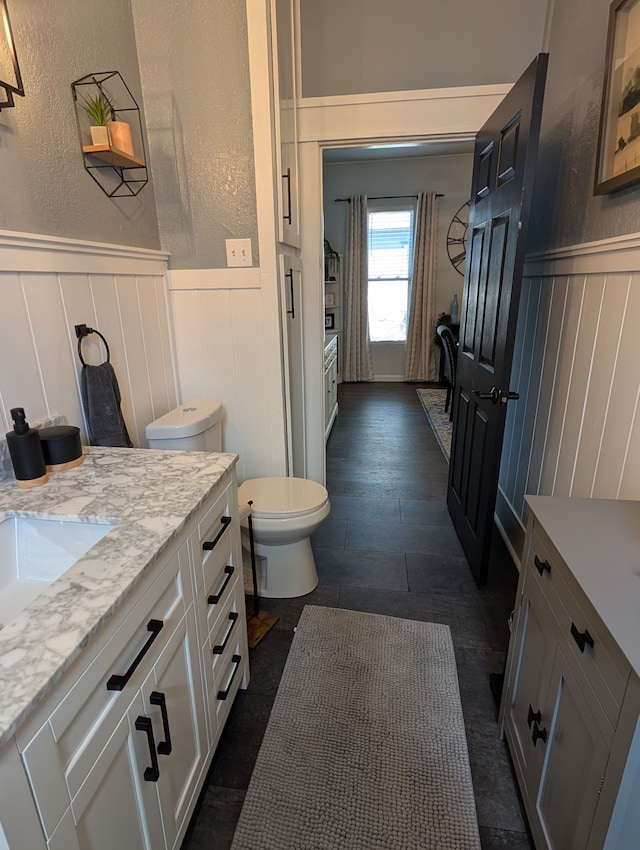 bathroom with a decorative wall, toilet, a wainscoted wall, and vanity