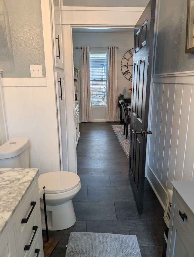 full bathroom with toilet, vanity, a wainscoted wall, and a decorative wall