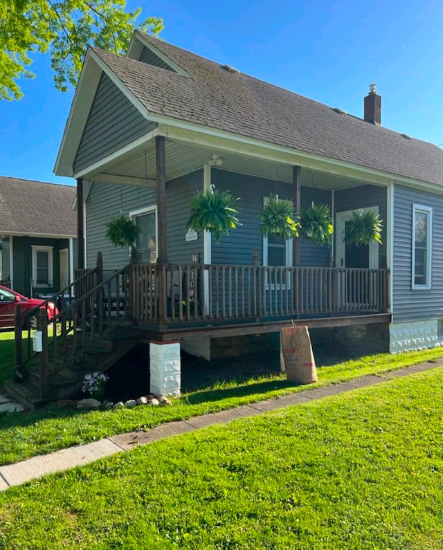 rear view of house featuring covered porch, a yard, and a shingled roof