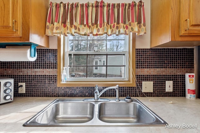 kitchen with brown cabinets, a sink, backsplash, and light countertops