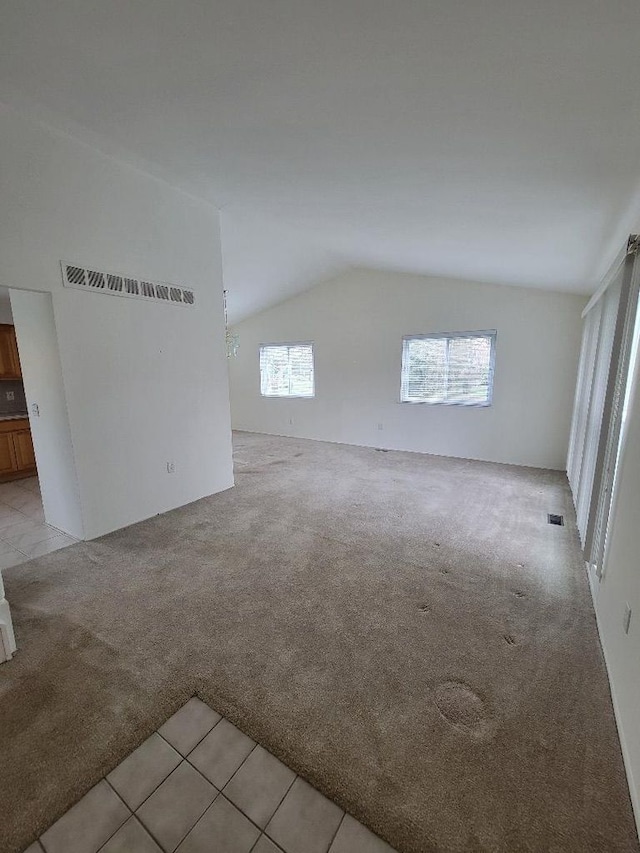 empty room featuring visible vents, light tile patterned floors, light carpet, and lofted ceiling