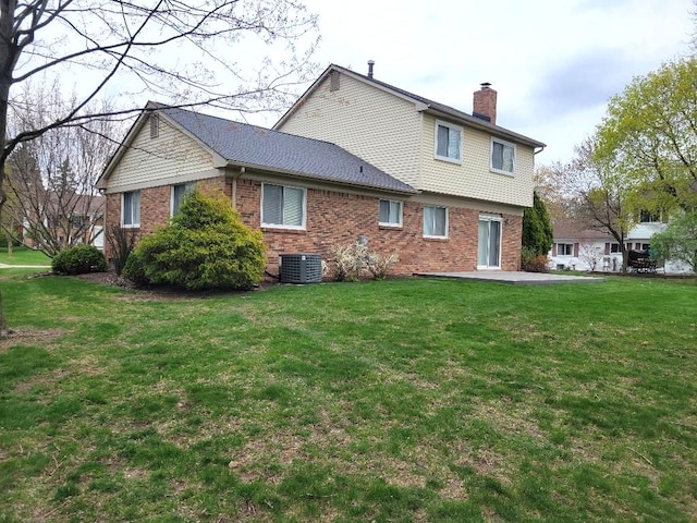 back of property featuring a chimney, brick siding, central air condition unit, a patio, and a lawn