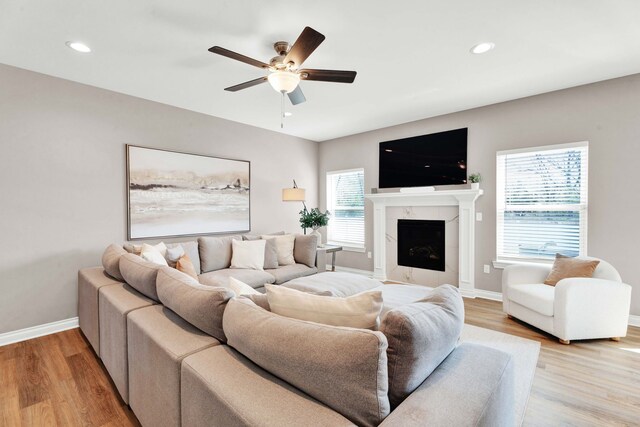 living room featuring baseboards, light wood-style floors, a high end fireplace, and a ceiling fan