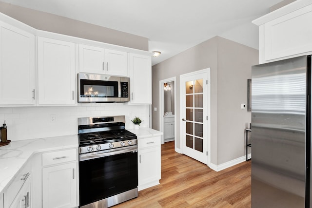 kitchen featuring tasteful backsplash, appliances with stainless steel finishes, light stone counters, white cabinets, and light wood-style floors