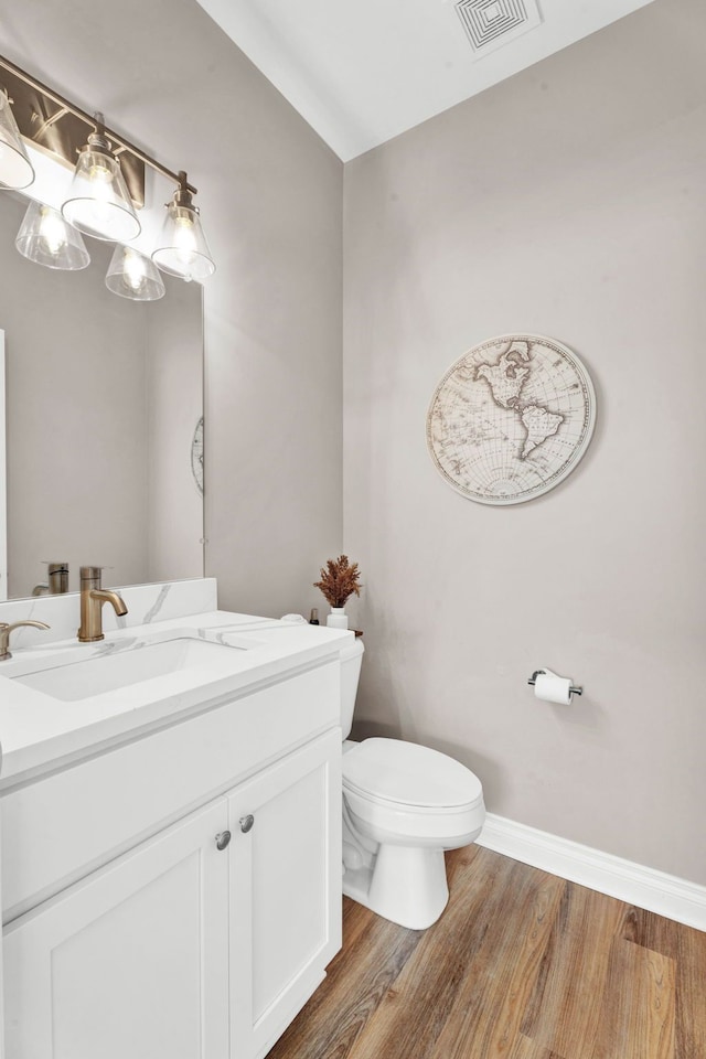 half bathroom with toilet, wood finished floors, visible vents, baseboards, and vanity