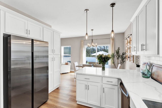 kitchen with light wood finished floors, a peninsula, a chandelier, white cabinets, and appliances with stainless steel finishes