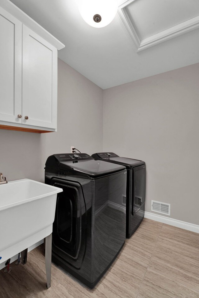 washroom featuring a sink, cabinet space, washer and clothes dryer, visible vents, and baseboards