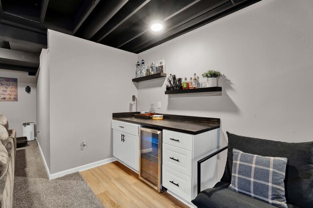 bar featuring light wood finished floors, beverage cooler, a dry bar, and baseboards